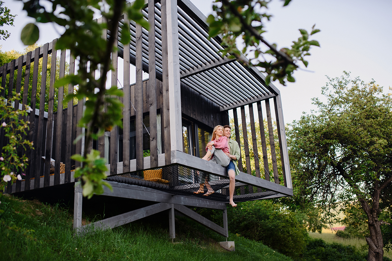 Young,Couple,Sitting,And,Cuddling,In,Hammock,Terrace,In,Their